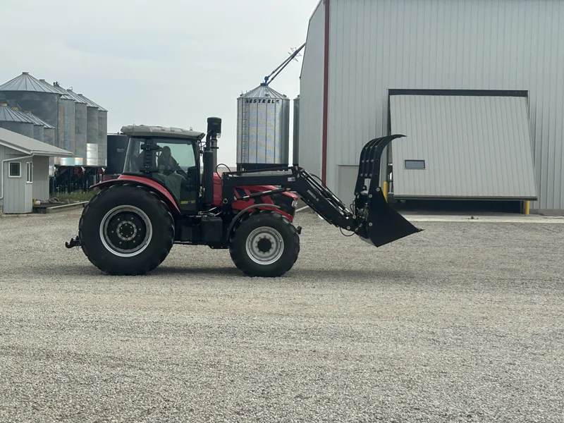URSA tractor and grapple bucket beside farm buildings
